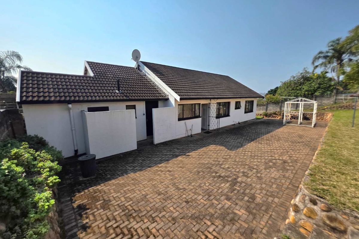 Rear view of the house featuring a tiled roof, paved patio area, and stone retaining wall in the garden.