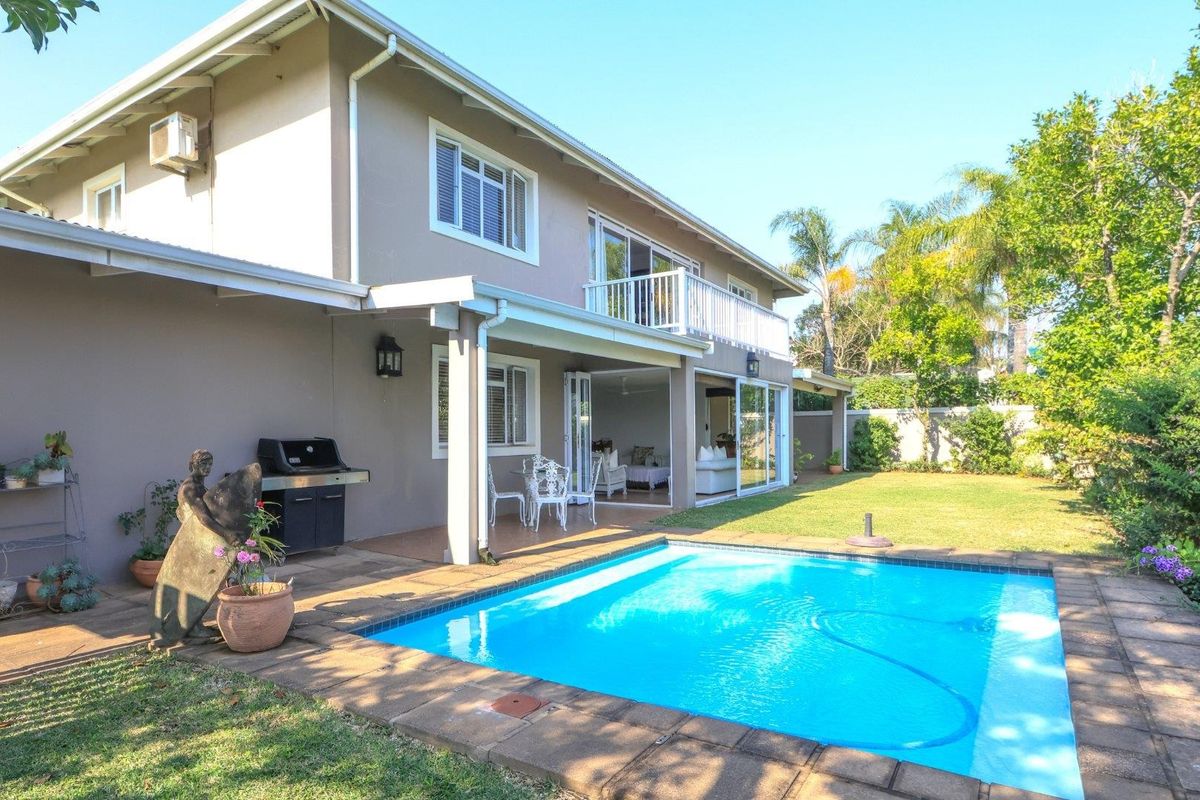 Rear view of a two-story house featuring a swimming pool, paved patio area, and a balcony overlooking the garden.