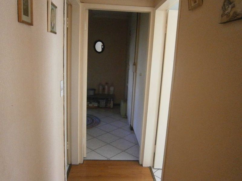 A narrow interior hallway connecting living spaces, featuring a mix of laminate and tiled flooring with a small circular porthole window.
