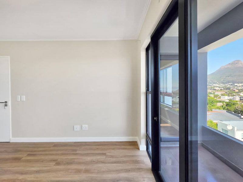 A bright, empty living area featuring modern laminate flooring and large sliding glass doors that open onto a balcony with scenic mountain views.