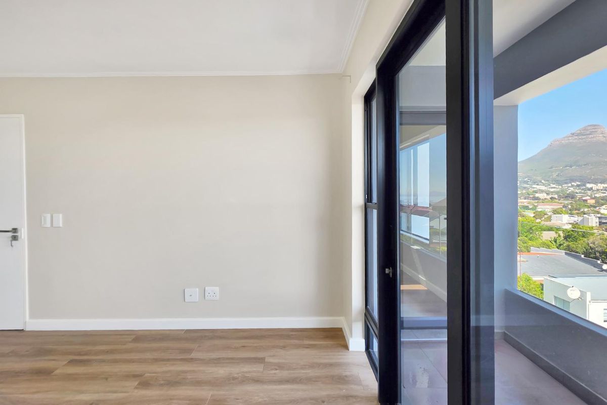 A bright, empty living area featuring modern laminate flooring and large sliding glass doors that open onto a balcony with scenic mountain views.