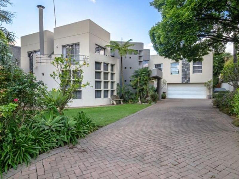 Front elevation of a modern multi-level house featuring a paved driveway, double garage, and established landscaped garden.
