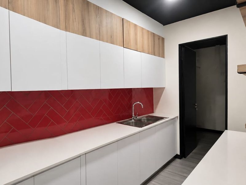 Modern office kitchenette featuring sleek white and wood-tone cabinetry, a striking red herringbone backsplash, stainless steel sink, and minimalist floating shelves.