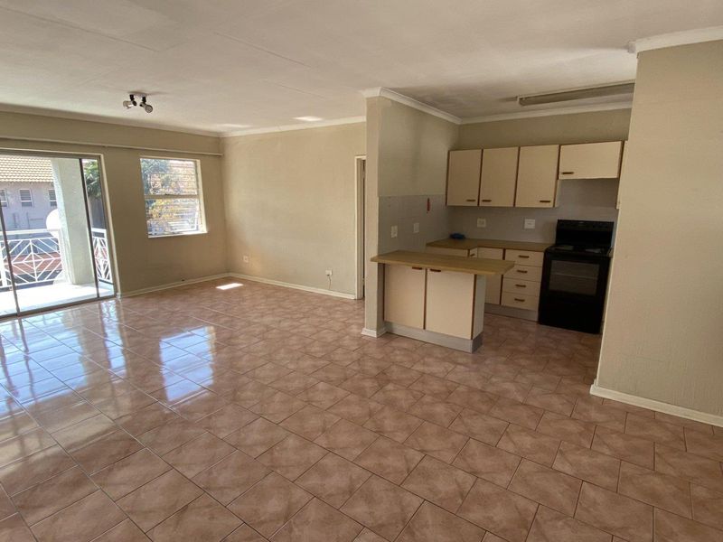 Open-plan living area featuring tiled floors, a compact kitchen with built-in cabinetry, and a sliding door leading to a private balcony.