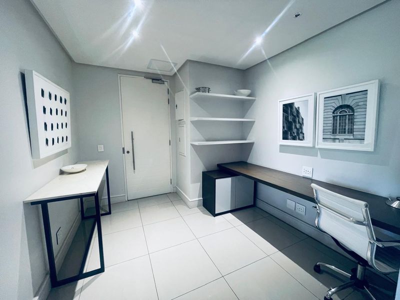 A modern, well-lit home office featuring a built-in desk, floating shelving, and neutral tiled flooring, providing a clean and functional workspace.