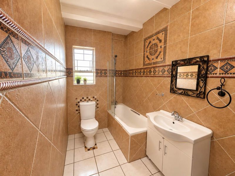 A functional bathroom featuring a bathtub with a glass screen, a vanity cabinet with a basin, and a toilet, finished with decorative wall tiling.