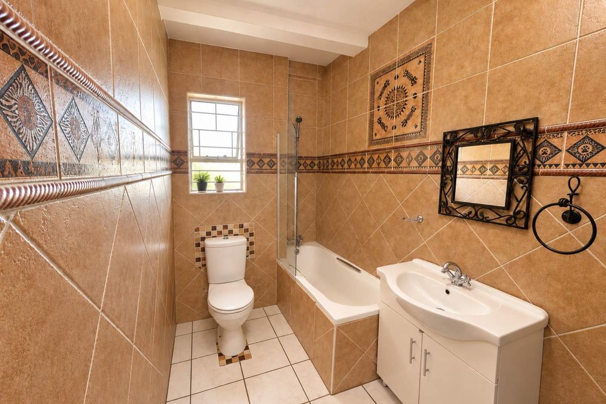 A functional bathroom featuring a bathtub with a glass screen, a vanity cabinet with a basin, and a toilet, finished with decorative wall tiling.