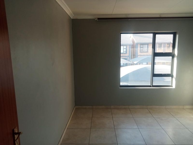An empty bedroom featuring neutral grey walls, tiled flooring, and an aluminium-framed window.