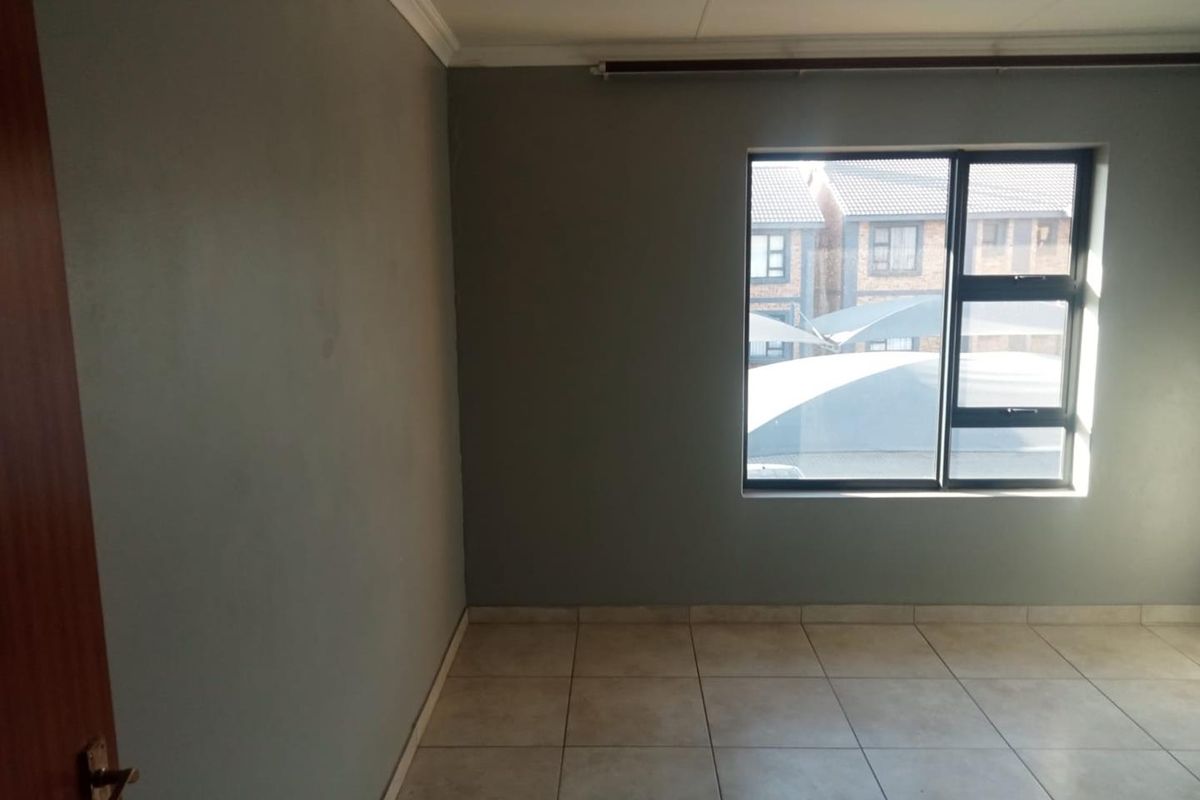 An empty bedroom featuring neutral grey walls, tiled flooring, and an aluminium-framed window.