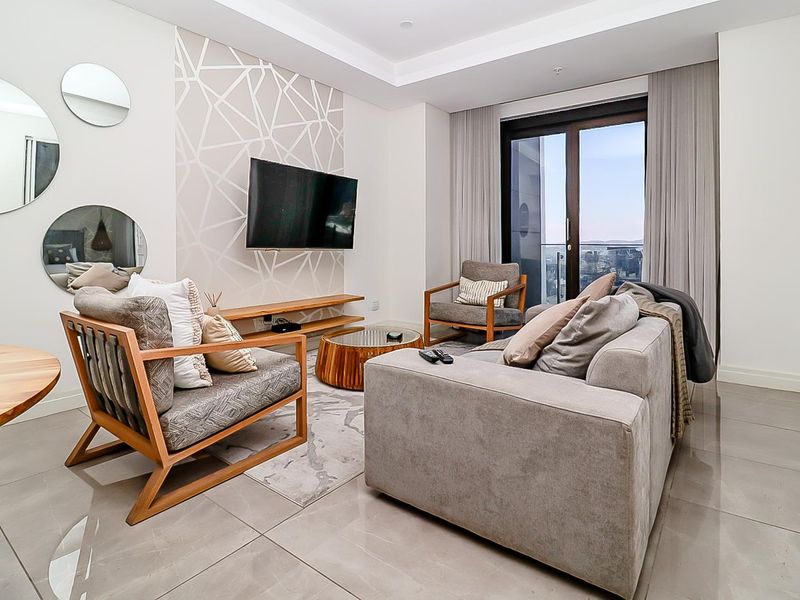 Modern living room featuring large format floor tiles, recessed ceiling lighting, a floating media shelf, and direct access to a private balcony.