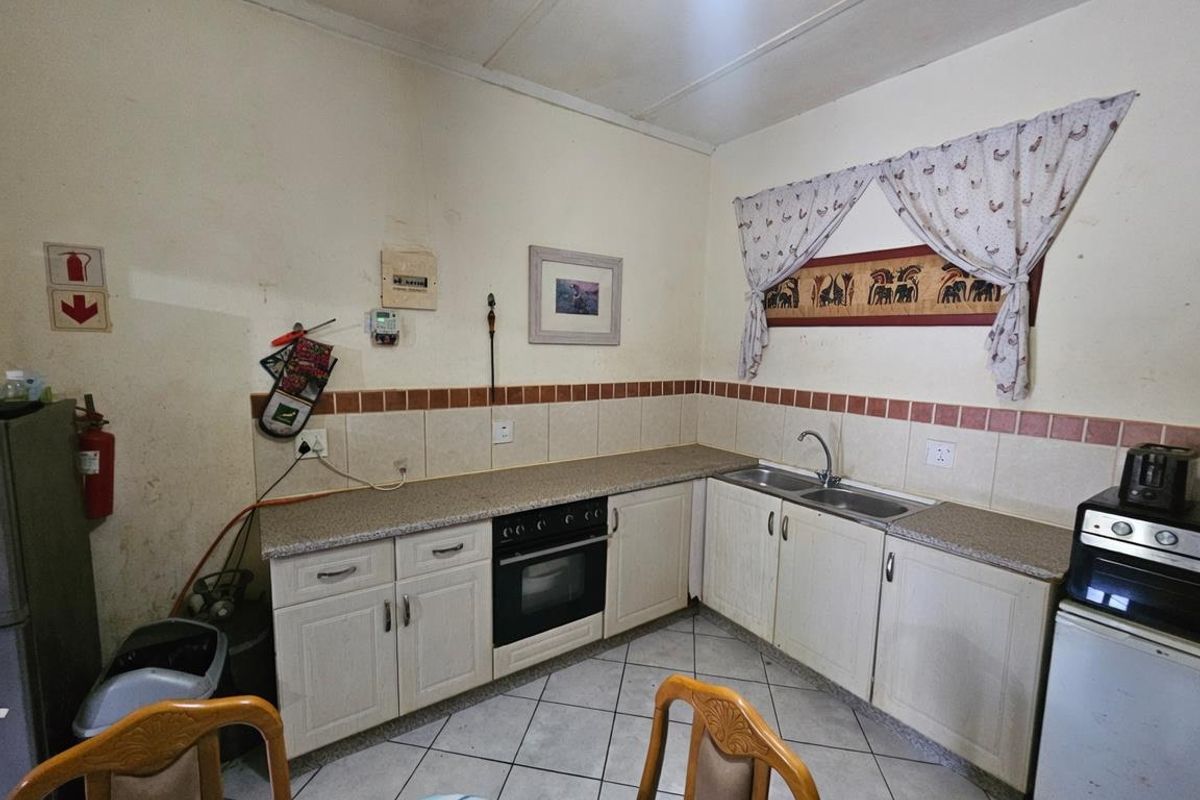 A dated kitchen featuring laminate countertops, built-in oven, and double sink with tiled splashbacks and ceramic floor tiles.