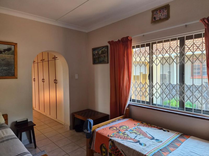 A bedroom featuring tiled flooring, built-in cupboards, and a window fitted with a security gate, providing a functional and secure living space.