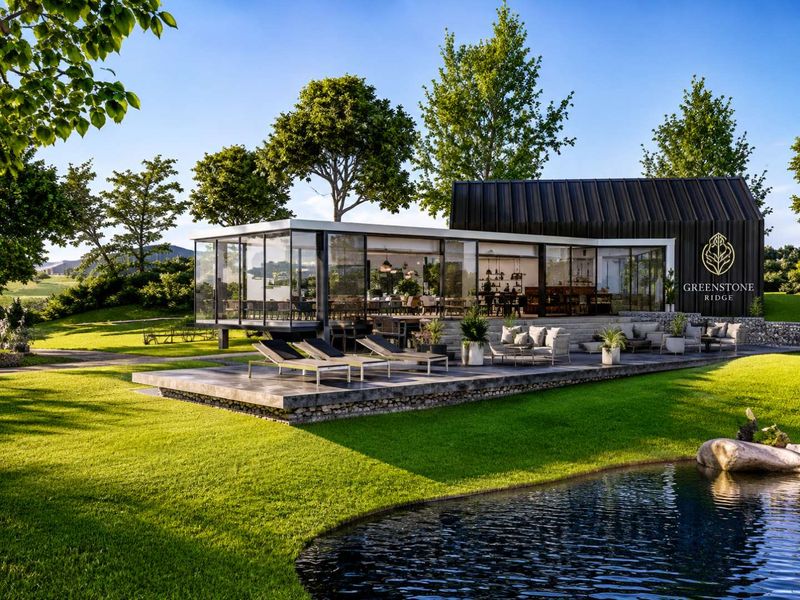 Modern clubhouse facility featuring floor-to-ceiling glass walls, a stone-clad terrace, and landscaped grounds with a water feature.