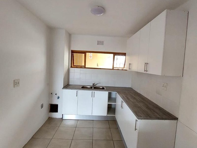 A clean, empty kitchen featuring white cabinetry, wood-look laminate countertops, tiled flooring, and a stainless steel sink, ready for personalization.