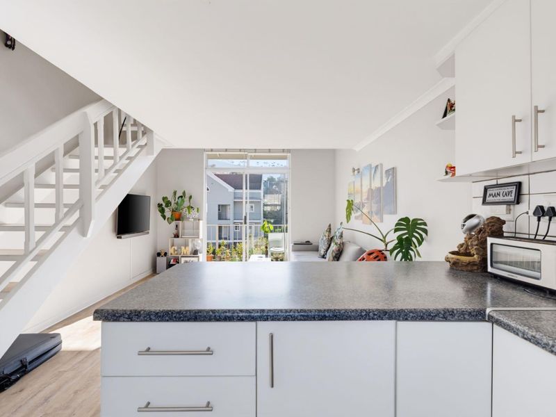 Open-plan living area featuring a modern kitchen with laminate countertops, tiled backsplash, and a staircase leading to the upper level.