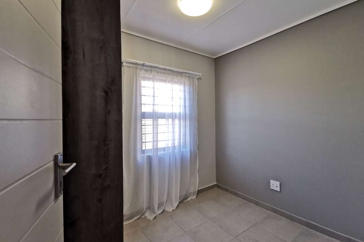 A clean, empty bedroom featuring neutral grey walls, tiled flooring, and a window fitted with security bars.