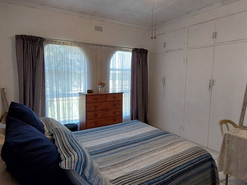A bedroom featuring built-in cupboards, a ceiling fan, and distinctive arched windows, offering a functional space with potential for cosmetic updates.