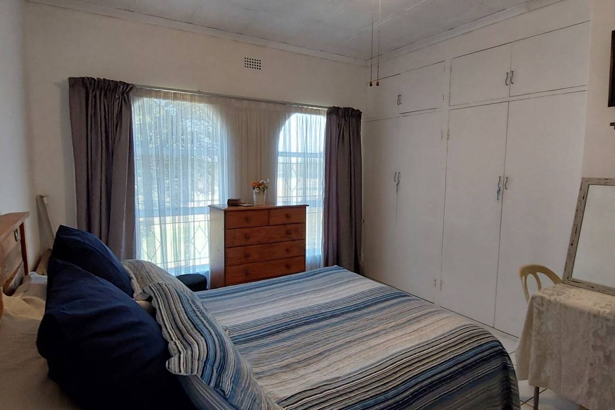 A bedroom featuring built-in cupboards, a ceiling fan, and distinctive arched windows, offering a functional space with potential for cosmetic updates.