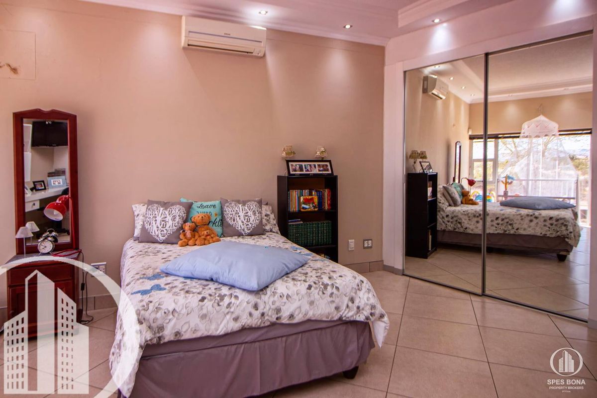 A well-maintained bedroom featuring tiled flooring, recessed ceiling lighting, a wall-mounted air conditioning unit, and large mirrored sliding wardrobe doors.