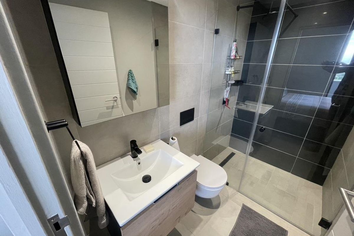 Modern bathroom featuring a wall-mounted vanity with integrated basin, wall-hung toilet, and a spacious walk-in shower with glass enclosure and contemporary tiling.