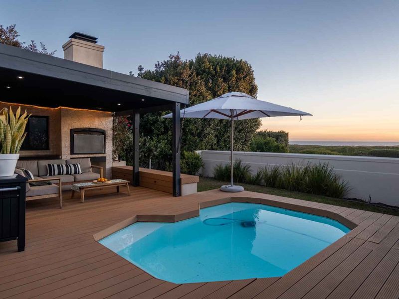 Outdoor entertainment area featuring a swimming pool, composite decking, and a covered patio with a built-in fireplace, offering scenic coastal views.