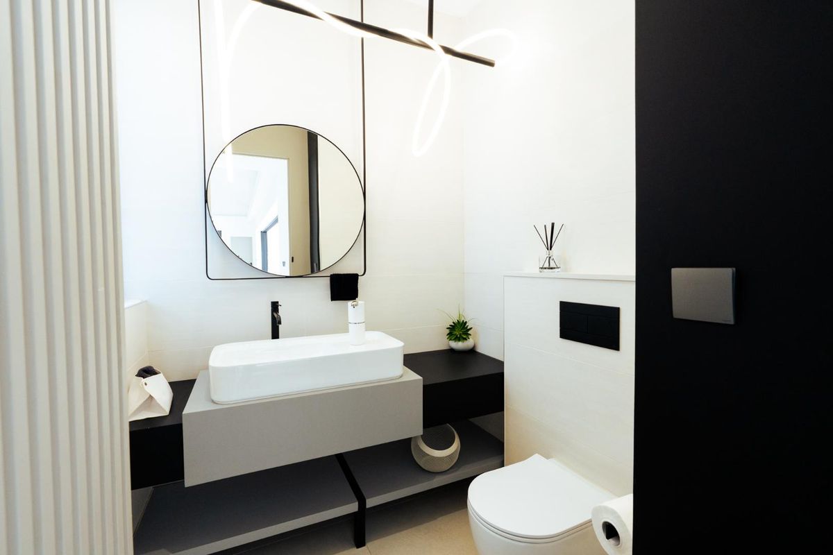 Modern bathroom featuring a sleek wall-mounted vanity with a vessel sink, circular mirror, and a concealed cistern toilet with matte black fixtures.