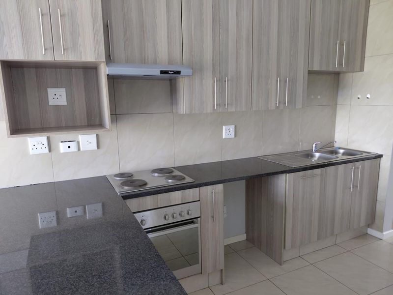 Modern kitchen featuring light wood-grain cabinetry, dark granite countertops, built-in oven, electric hob, extractor fan, and a double bowl sink with tiled backsplash.
