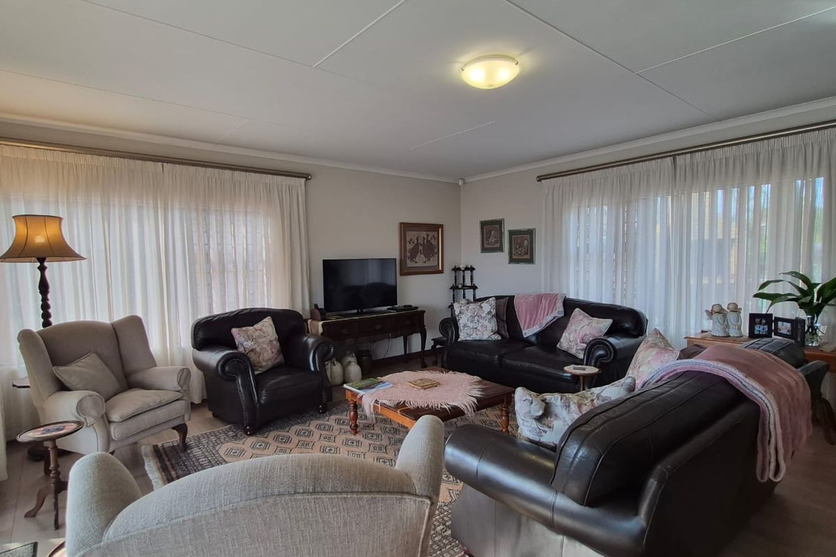 A spacious living room featuring large windows with sheer curtains, providing ample natural light and a comfortable, traditional layout.