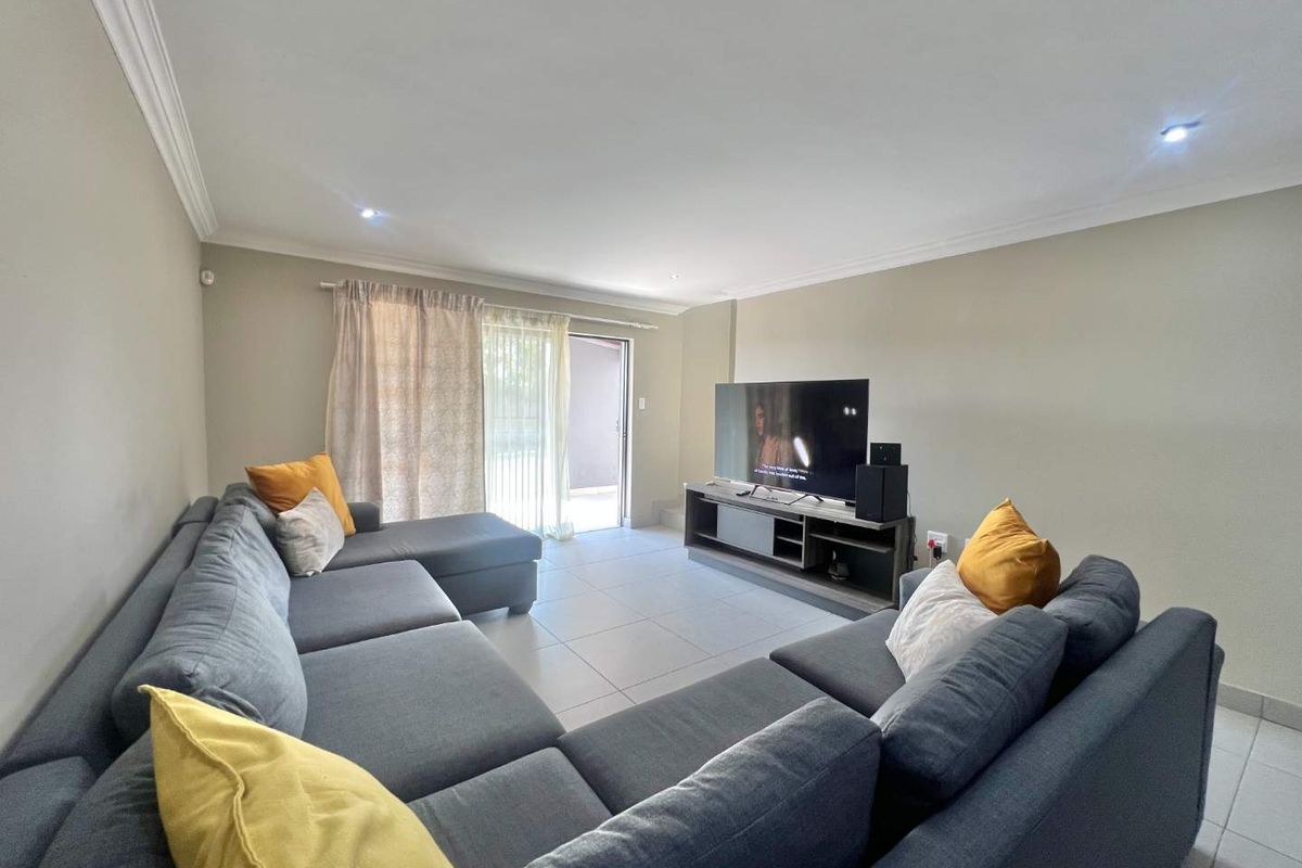 A well-maintained living room featuring tiled flooring, recessed downlighting, and a sliding glass door providing access to the outdoor area.