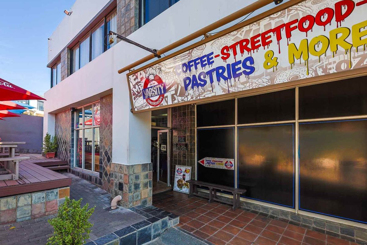 Front facade of a commercial street food cafe featuring stone cladding, large signage, and an adjacent outdoor timber deck seating area.