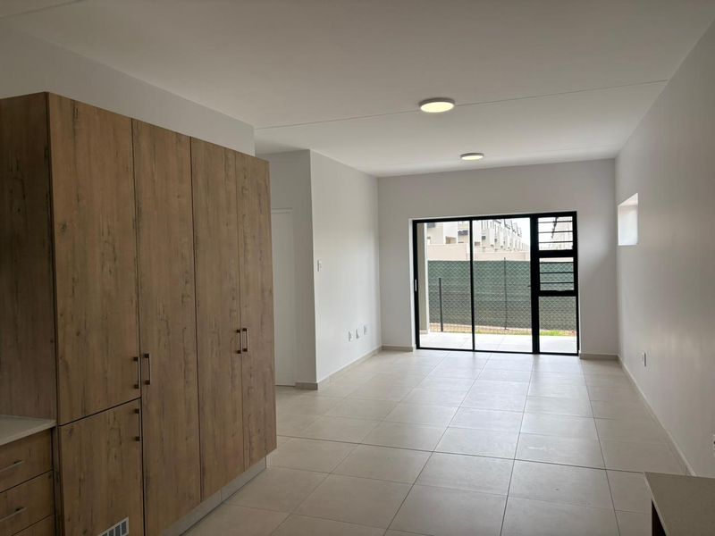 An open-plan living area featuring neutral tiled flooring, modern wood-finish built-in cabinetry, and a large sliding glass door leading to an outdoor space.