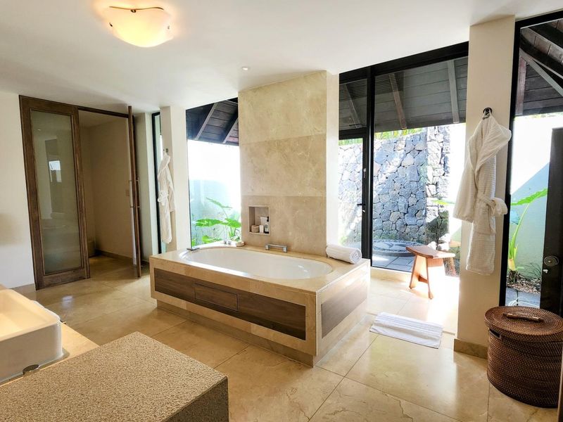Luxurious bathroom featuring a central built-in bathtub, double vanity, stone finishes, and large glass doors opening to a private outdoor area.
