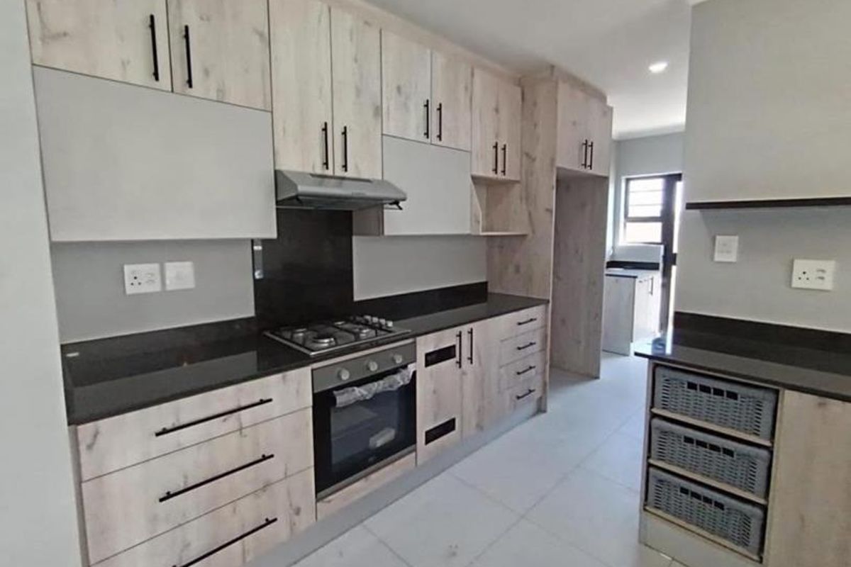 Modern kitchen featuring light wood-grain cabinetry, dark stone countertops, integrated gas hob, electric oven, and extractor fan with neutral tiled flooring.
