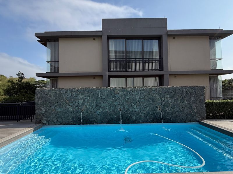 A well-maintained swimming pool area featuring a stone water feature wall, modern decking, and a view of the apartment building's rear facade.