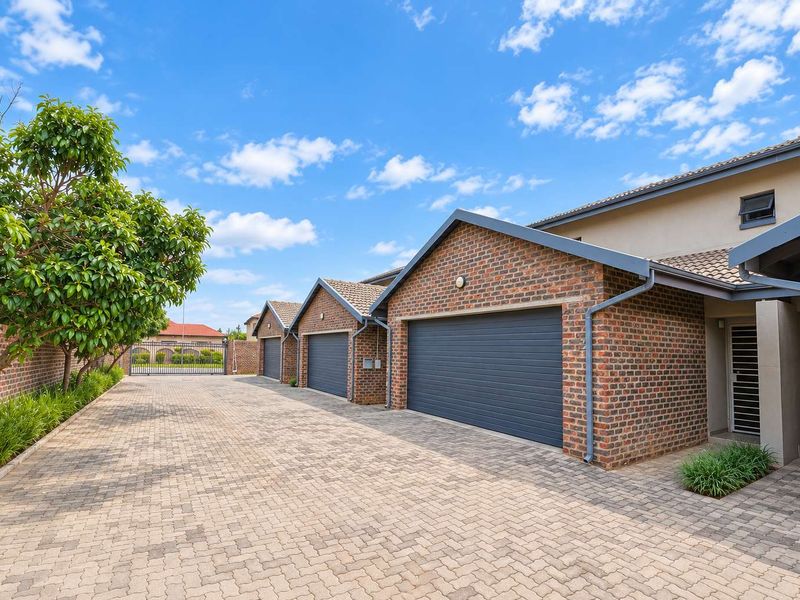A well-maintained townhouse exterior featuring a paved driveway and multiple secure garage bays with brick facade detailing.
