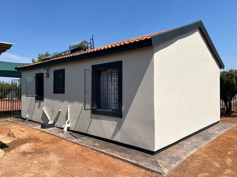 Rear view of a well-maintained house featuring a tiled roof, solar water heater, and concrete apron surrounding the exterior walls.