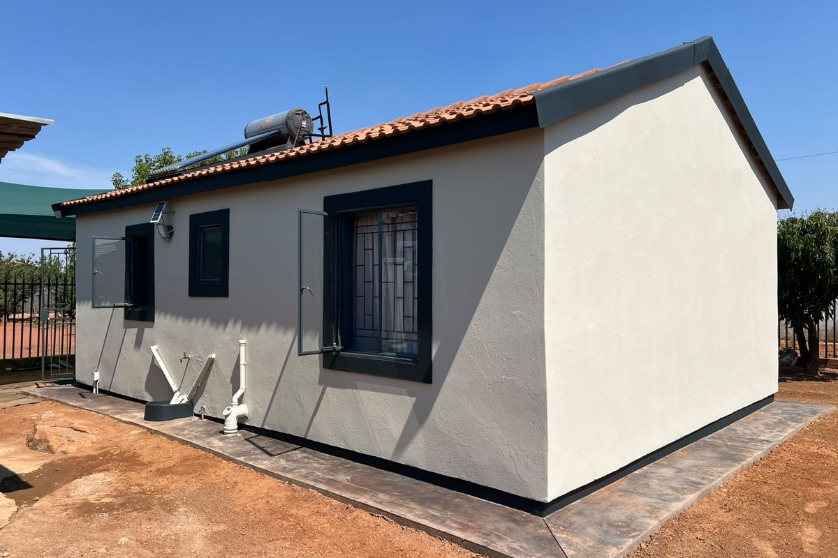 Rear view of a well-maintained house featuring a tiled roof, solar water heater, and concrete apron surrounding the exterior walls.