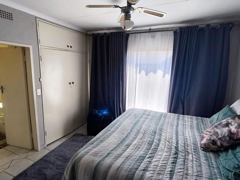 A bedroom featuring built-in cupboards, a ceiling fan, and tiled flooring, with an adjoining bathroom visible through the doorway.
