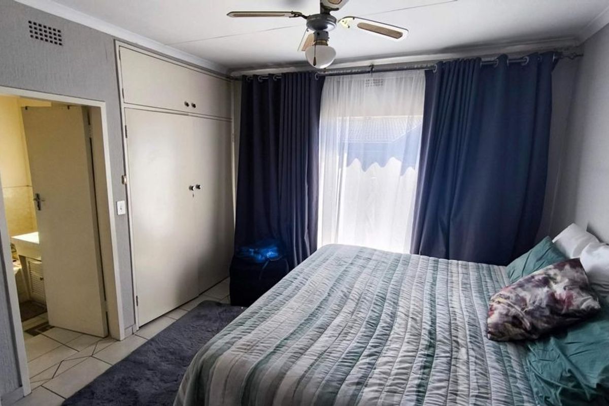 A bedroom featuring built-in cupboards, a ceiling fan, and tiled flooring, with an adjoining bathroom visible through the doorway.
