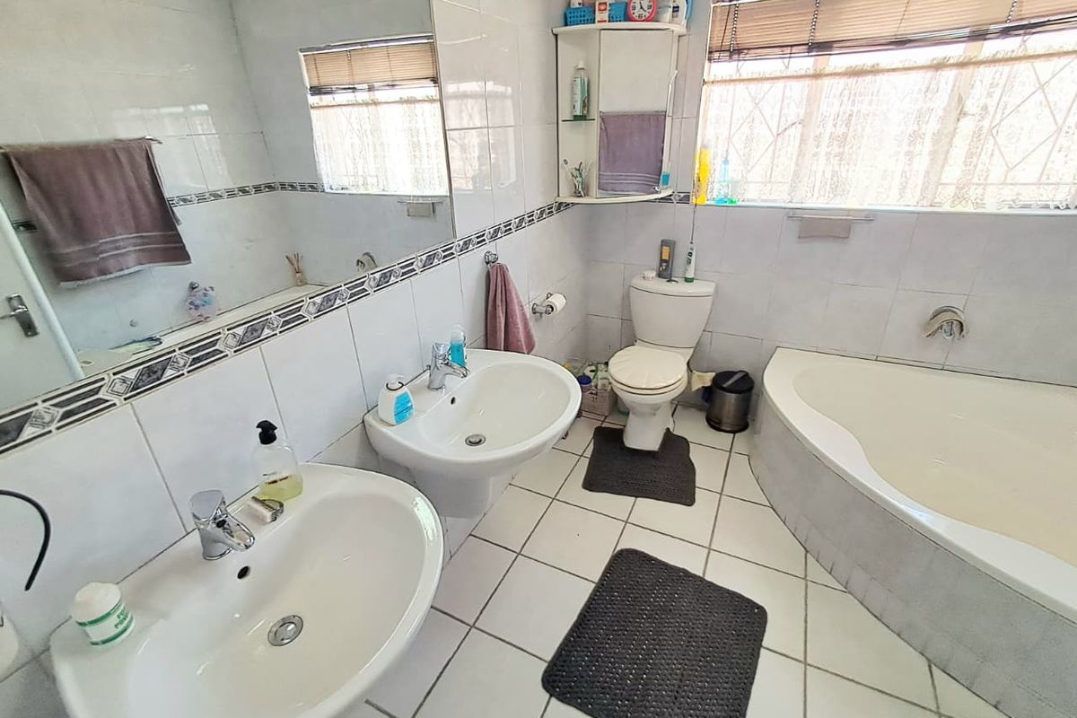 A functional bathroom featuring dual vanity basins, a corner bathtub, a toilet, and tiled finishes throughout, offering a practical layout for daily use.