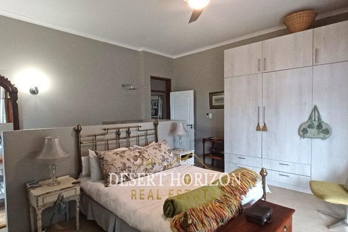 Spacious bedroom featuring built-in wardrobes and an open-plan vanity area with a wall-mounted mirror and basin.