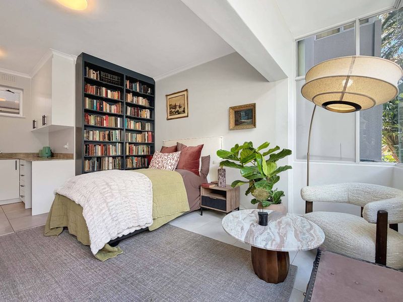 An open-plan living and sleeping area featuring a built-in bookshelf, tiled flooring, and large windows that provide ample natural light.