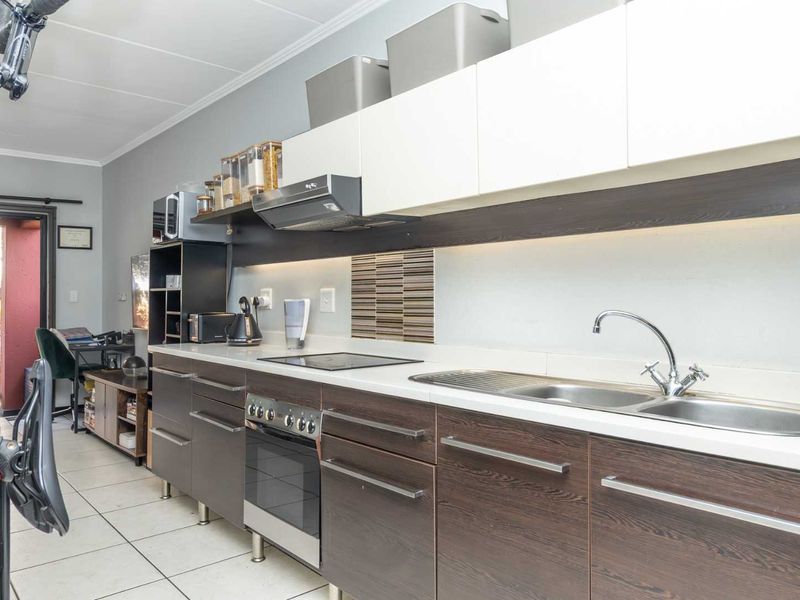 A functional kitchen featuring dark wood-finish cabinetry, white countertops, a stainless steel sink, and integrated cooking appliances with modern under-cabinet lighting.