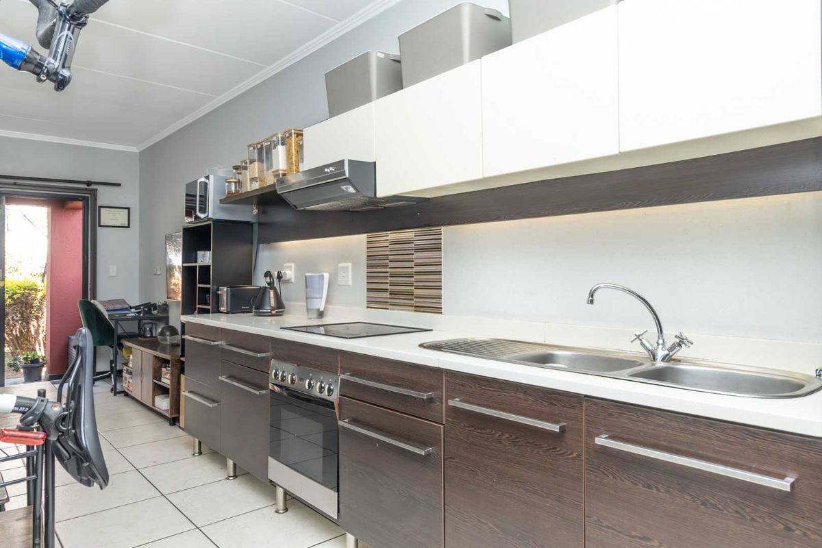 A functional kitchen featuring dark wood-finish cabinetry, white countertops, a stainless steel sink, and integrated cooking appliances with modern under-cabinet lighting.