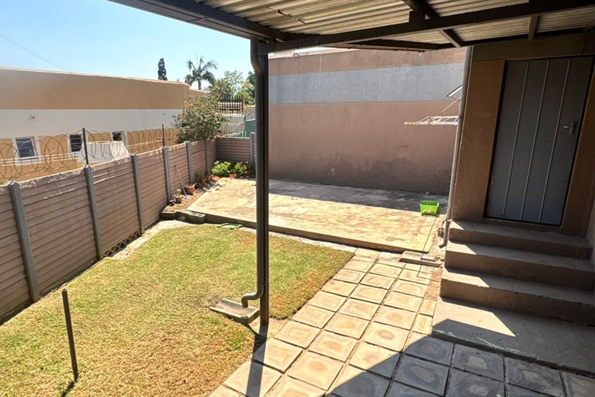 Rear exterior area featuring a covered patio with corrugated metal roofing, paved flooring, concrete steps, and a small private garden enclosed by precast walling.