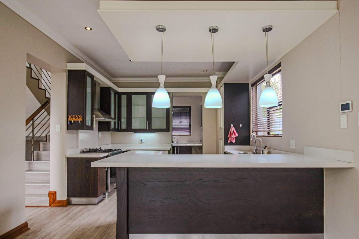 Modern kitchen featuring dark wood cabinetry, stone countertops, a breakfast bar, and integrated stainless steel appliances, with an adjacent staircase visible.