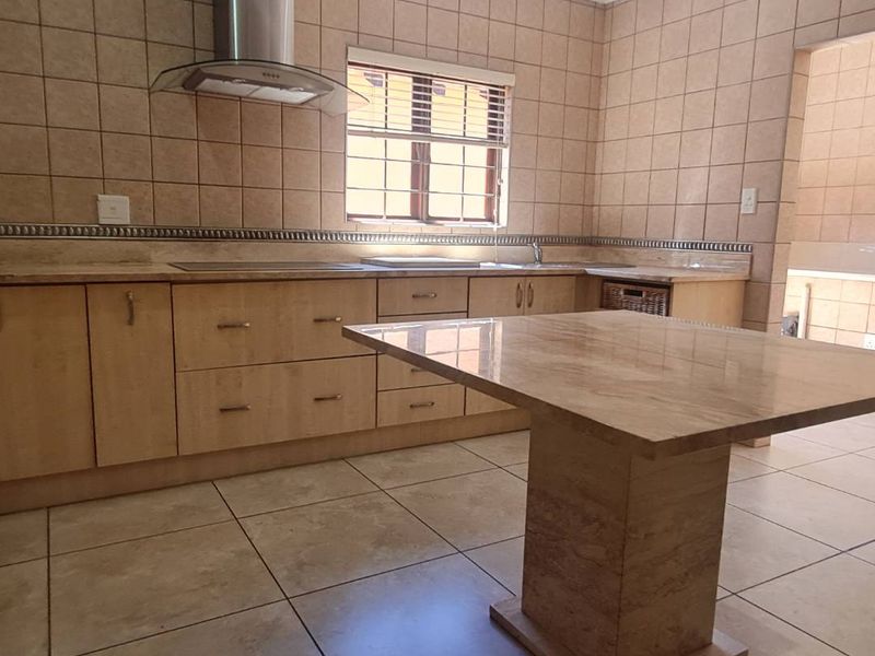 A spacious kitchen featuring built-in wooden cabinetry, stone countertops, a central island, and a stainless steel extractor fan, finished with neutral wall and floor tiles.