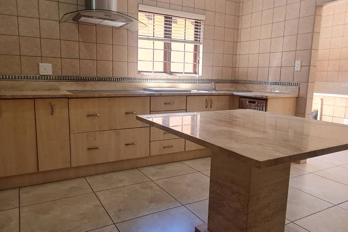 A spacious kitchen featuring built-in wooden cabinetry, stone countertops, a central island, and a stainless steel extractor fan, finished with neutral wall and floor tiles.