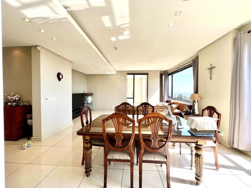 Spacious open-plan living and dining area featuring large format floor tiles, recessed ceiling lighting, and expansive windows with natural light.