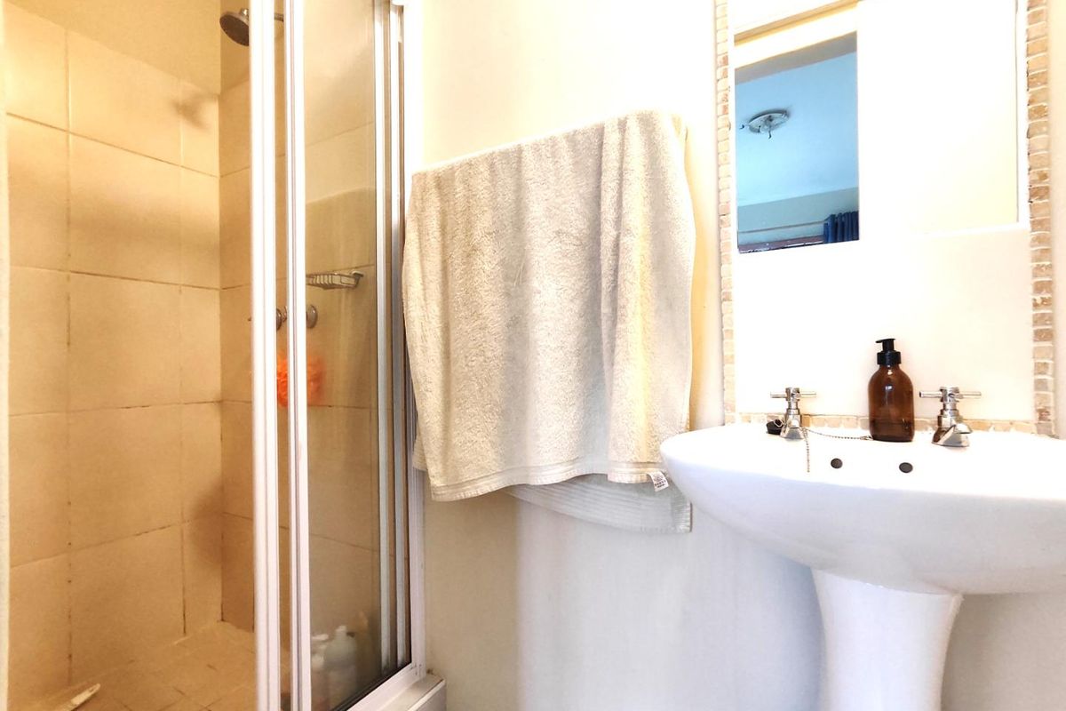 A functional bathroom featuring a shower enclosure with tiled walls and a classic pedestal sink with a wall-mounted mirror.